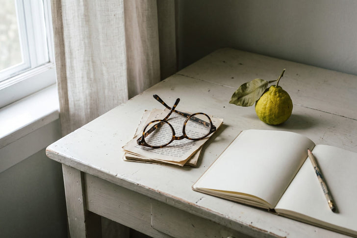Reading glasses, notebook and bergamot fruit on a desk